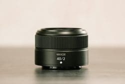 A Nikkor 40mm f/2 camera lens is placed upright on a flat surface against a neutral background. The focus is on the lens with clear labeling of the brand and specifications visible.