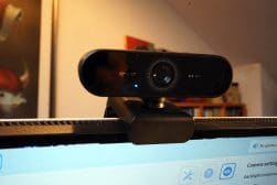 A black 4K webcam is mounted on top of a computer monitor, facing forward. The screen below displays camera settings options.