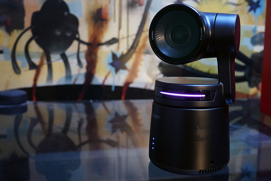 A black IBSBOT Tail Air camera with a rotating lens sits on a reflective surface.