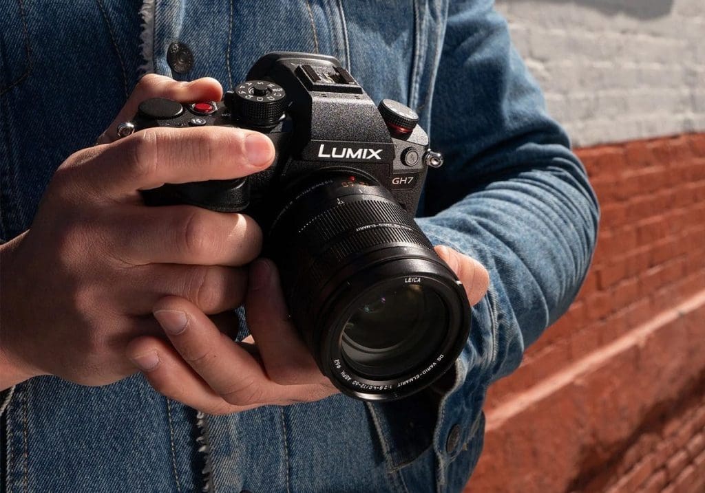 Person holding a Lumix GH7 camera outdoors with a denim jacket on.