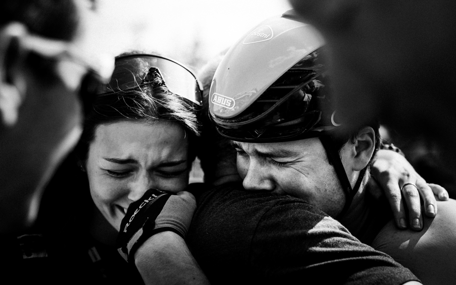 A black and white photo of an emotional embrace between a woman and a man wearing a helmet, both with tears in their eyes.