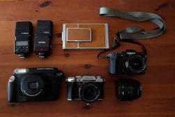 Assorted photography equipment on a wooden surface, including cameras, lenses, and flash units.