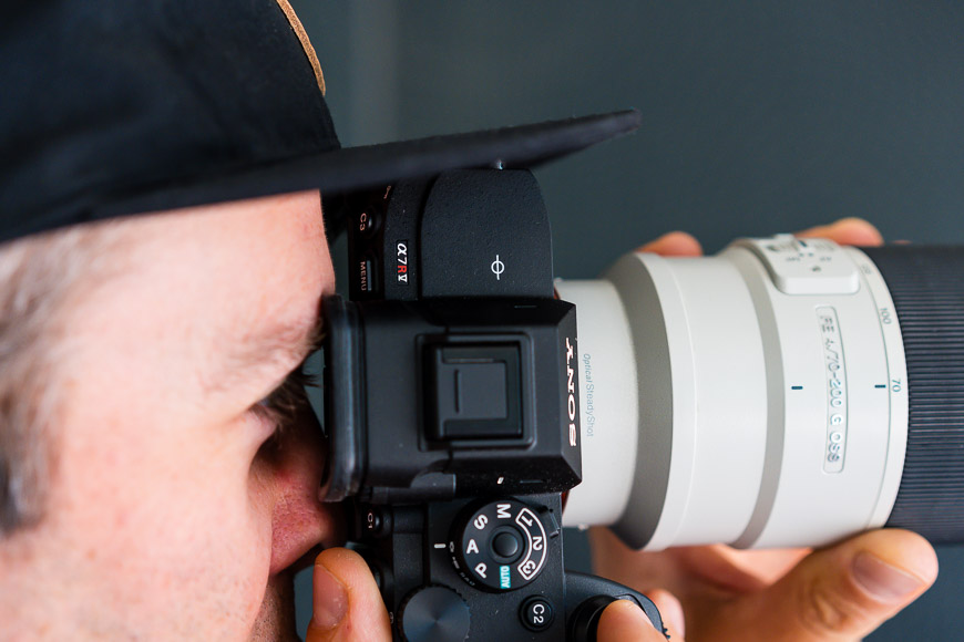 Close-up of a person using a Sony camera with a telephoto lens, focused intently through the viewfinder.