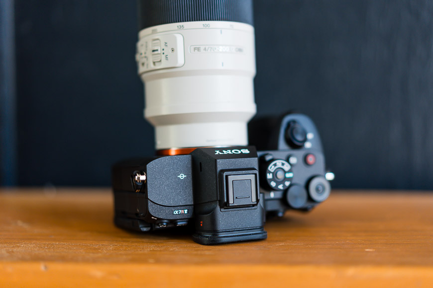 Close-up of a Sony camera with a large white zoom lens mounted on it, placed on a wooden surface.