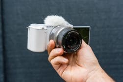 A hand holding a sony camera with a microphone attached to the top.