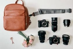Brown backpack, camera gear, flowers, and a keychain on a white surface.