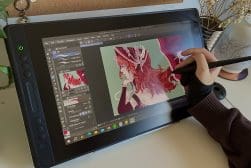 Artist's hand using a stylus on a graphics tablet to digitally paint an illustration.