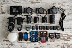 A collection of photography equipment displayed on a wooden surface, including cameras, lenses, flashes, and memory cards.