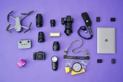 Photography and drone equipment arranged on a purple surface, including cameras, lenses, a drone, a controller, a laptop, a flash, and various accessories.