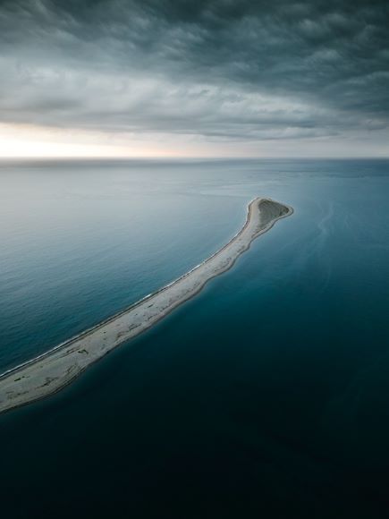 Aerial view of a narrow, elongated island surrounded by calm ocean under a cloudy sky.