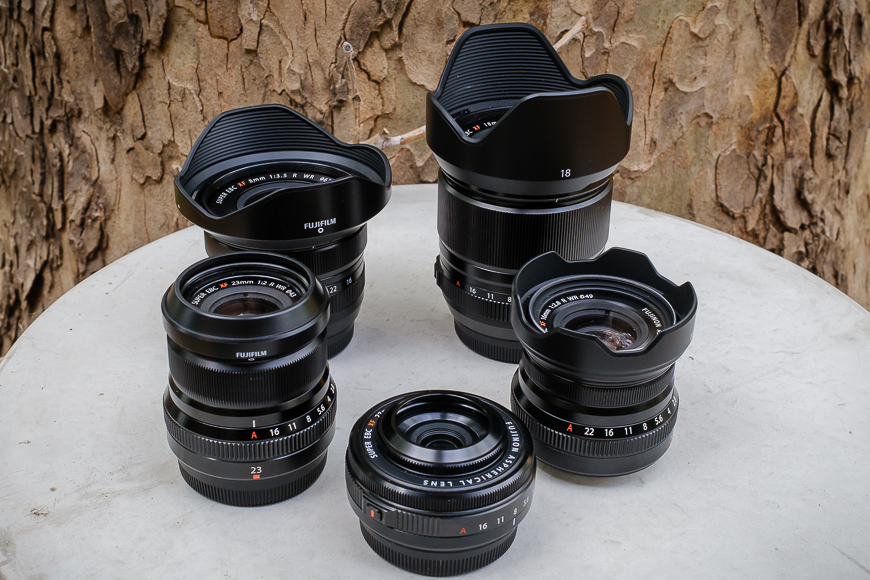 A collection of six camera lenses with varying focal lengths displayed on a surface with a tree bark background.