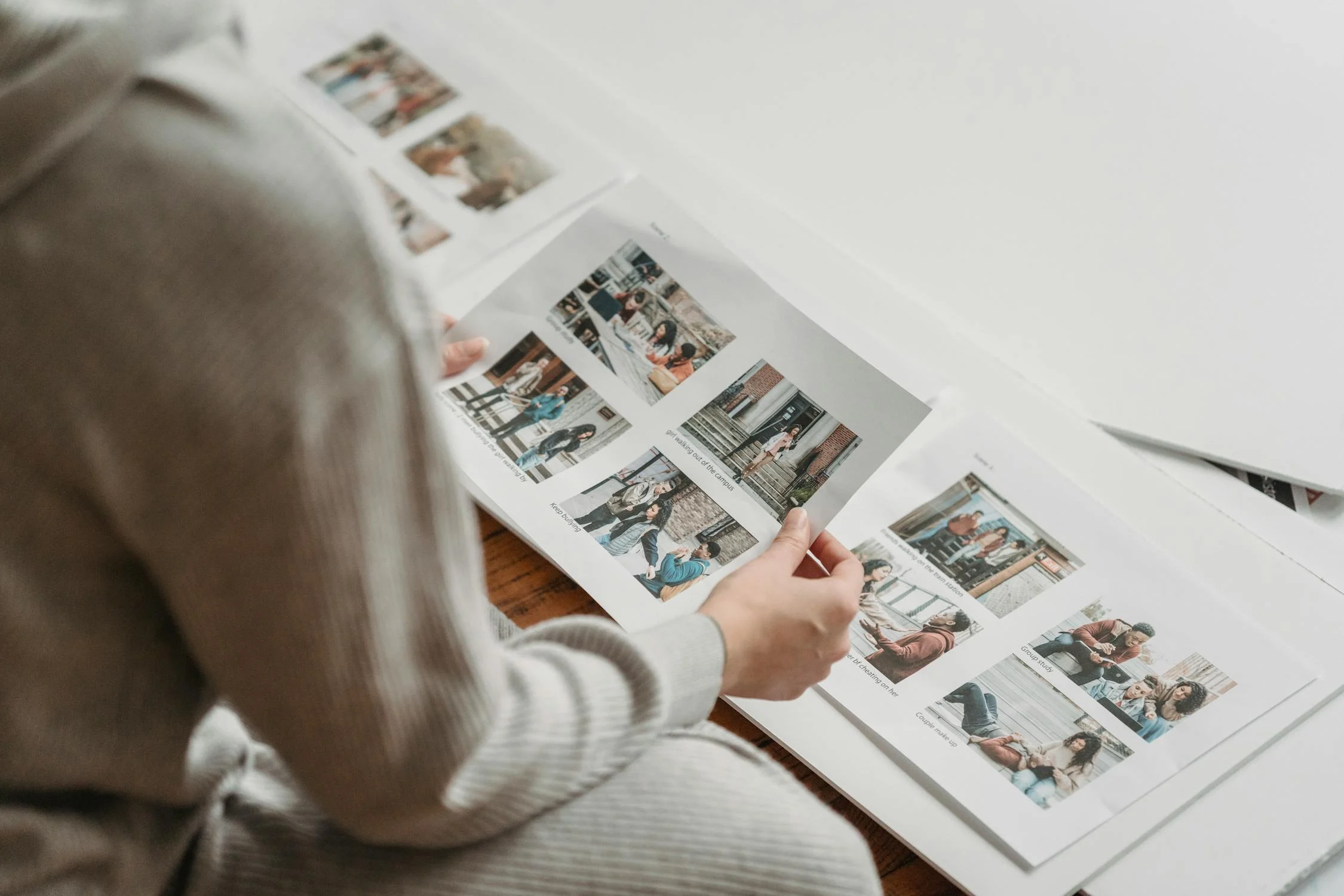 Person in a gray sweater looking at photo contact sheets on a table.