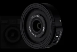 Close-up of a black camera lens with white markings, including "RS21/3.5" and "0.18m/0.59ft," against a dark background.
